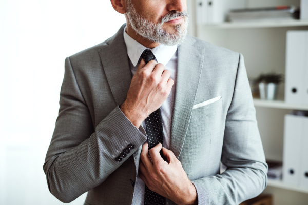 A midsection of unrecognizable mature businessman standing in an office, holding a tie.