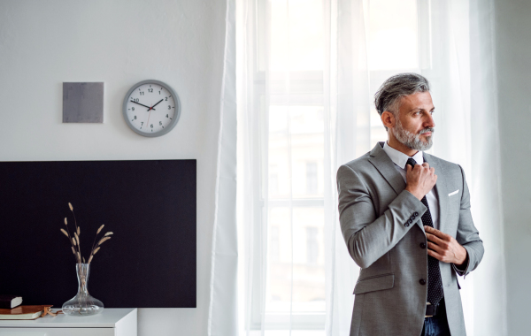 A serious mature businessman standing in an office, looking away. Copy space.