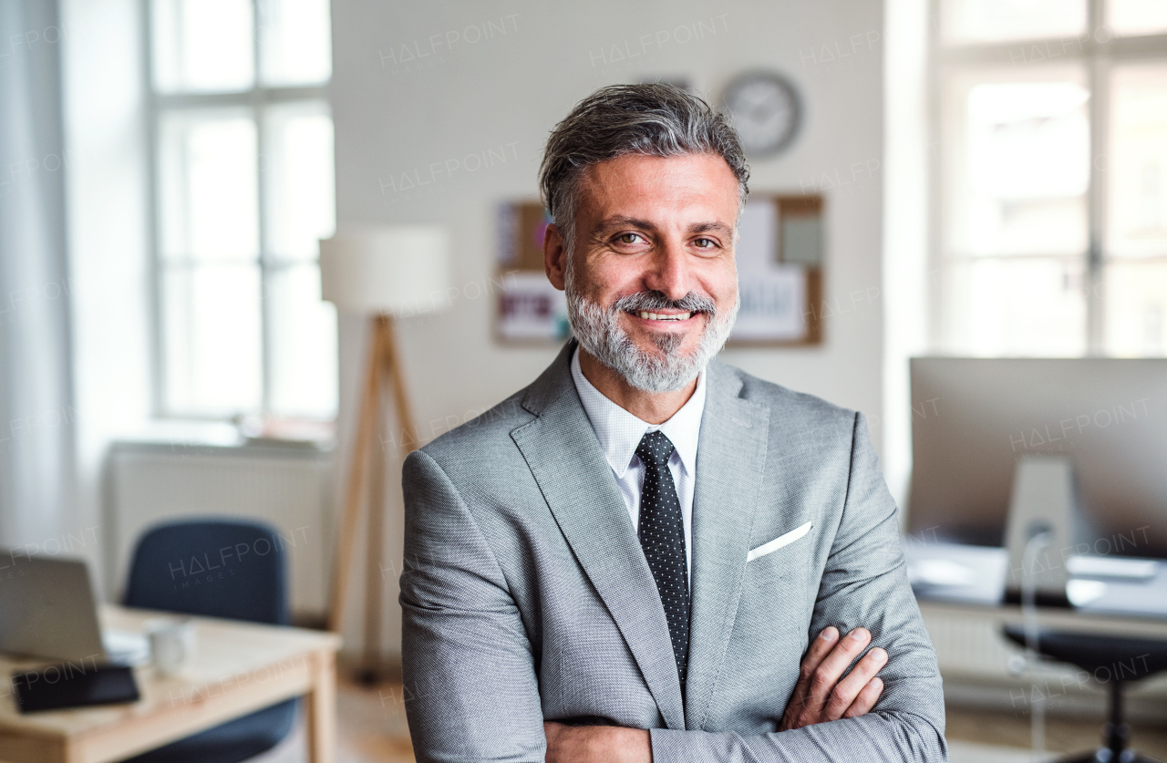 A cheerful mature businessman standing in an office, arms crossed.