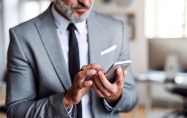 A midsection of unrecognizable businessman standing in an office, using smartphone.