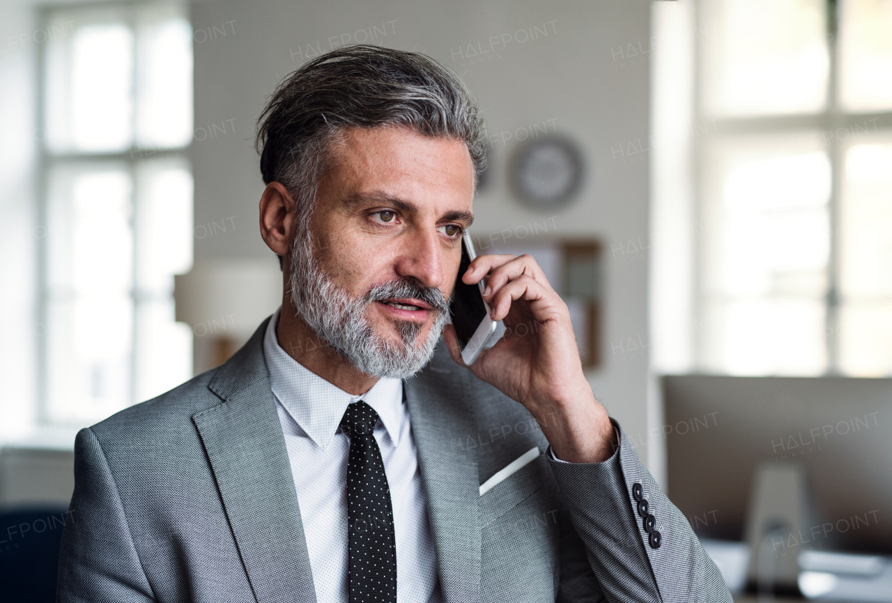 A serious mature businessman with smartphone in an office, making a phone call.