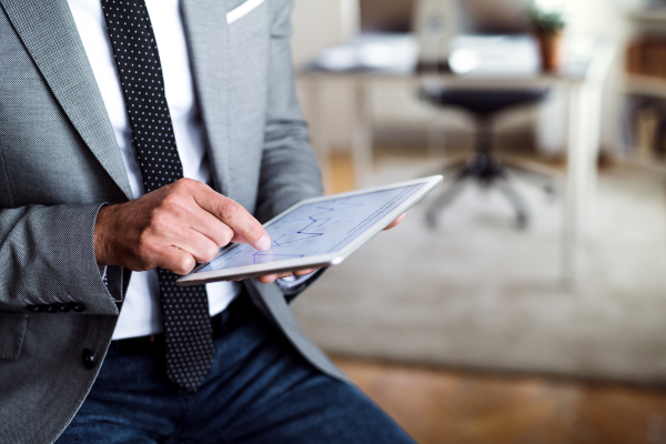 A midsection of unrecognizable businessman sitting in an office, using tablet. Copy space.