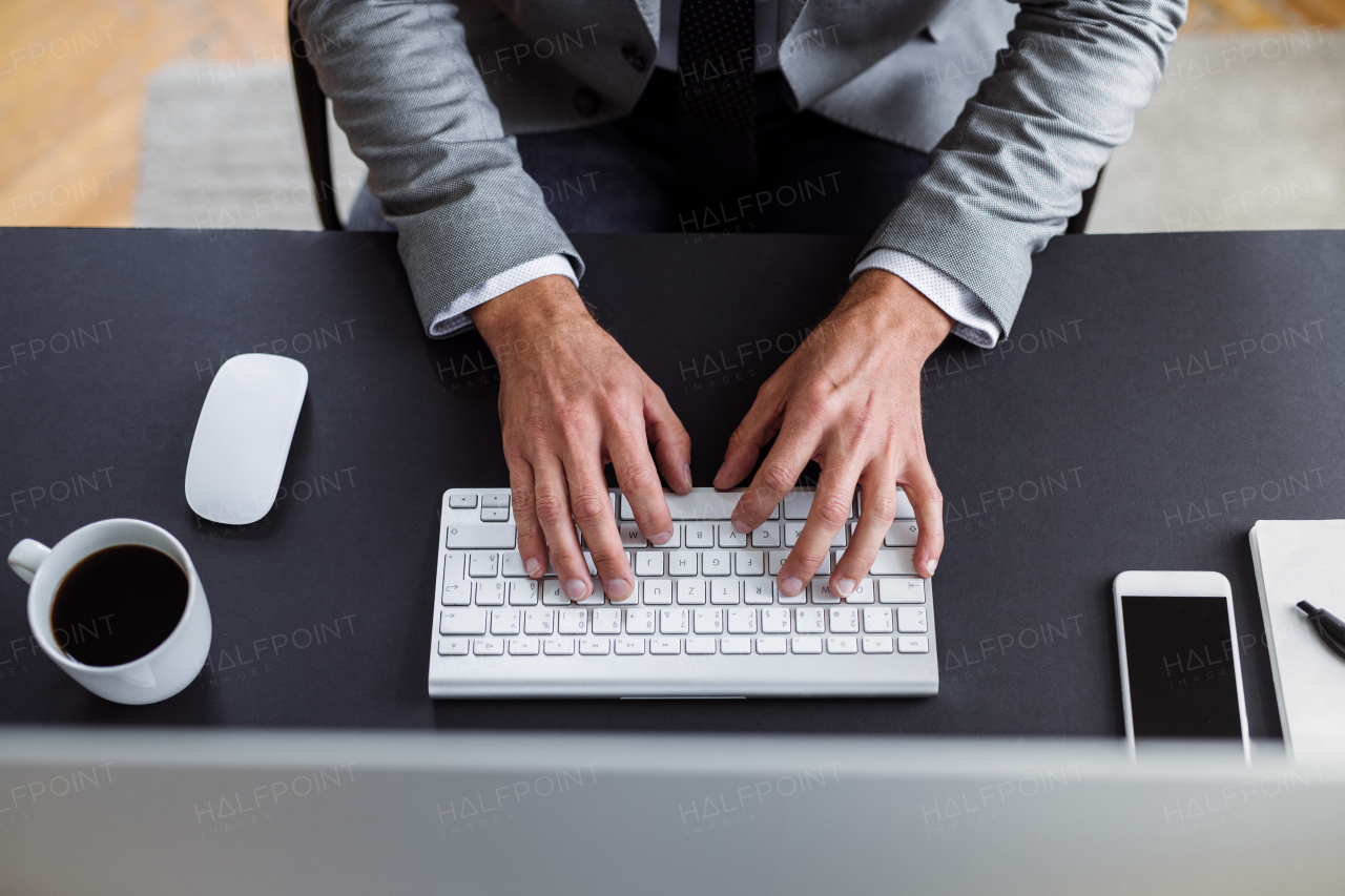 A midsection of businessman with computer sitting at the desk in an office, working. A top view.