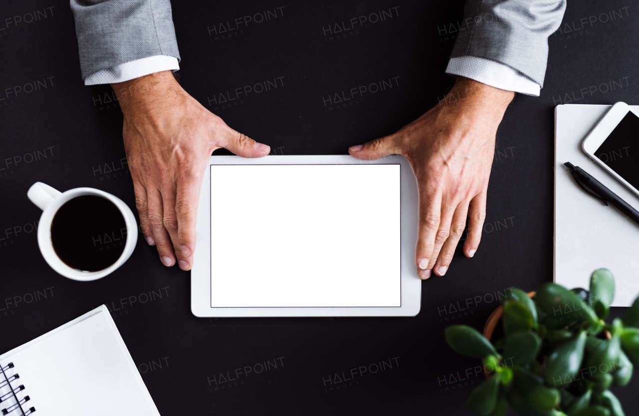 A midsection of unrecognizable businessman sitting at the table, using tablet. A top view. Copy space.