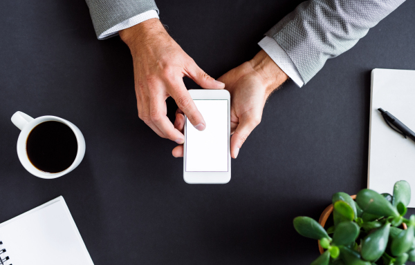 A midsection of unrecognizable businessman sitting at the table, using smartphone. A top view. Copy space.