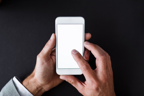 A top view of male hands holding smartphone on a desk. A copy space.