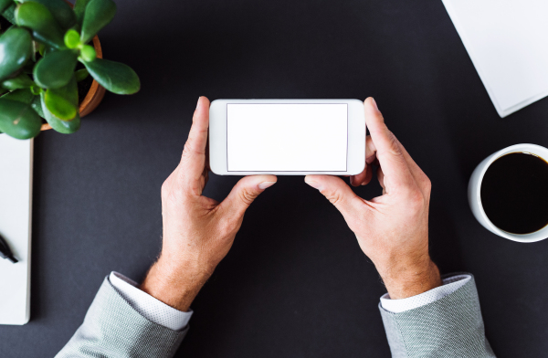 A midsection of unrecognizable businessman sitting at the table, using smartphone. A top view. Copy space.