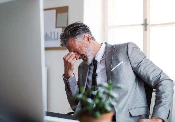 An unhappy and frustrated businessman sitting at the desk in an office, hearing bad news.