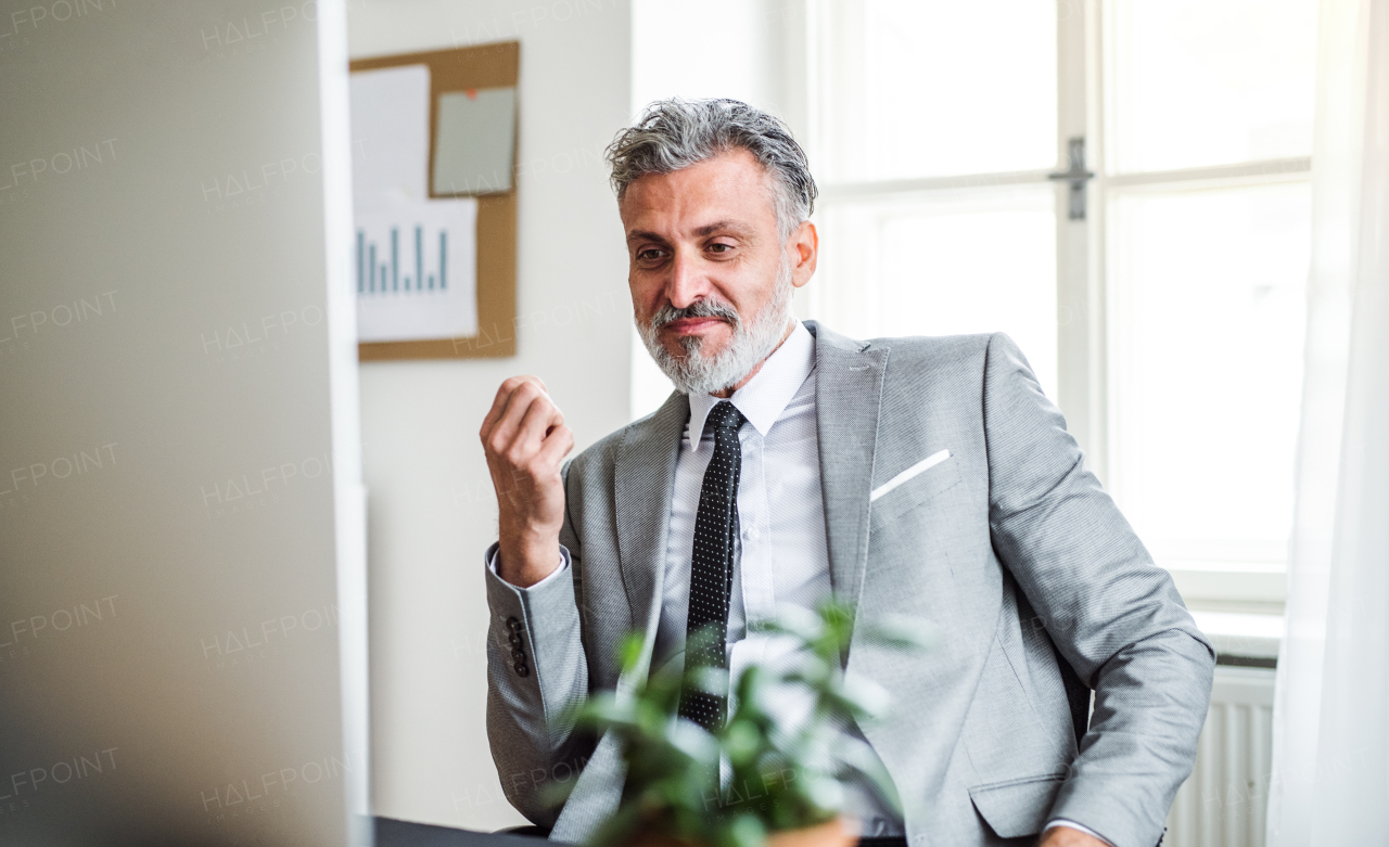 A serious mature businessman sitting at the table in an office. Copy space.