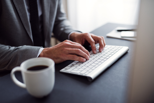 A midsection of businessman with computer sitting at the desk in an office, working.