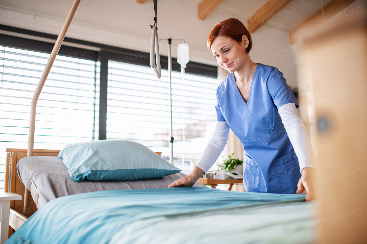 A portrait of female nurse or housekeeping staff changing sheets in hospital.