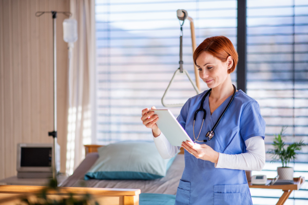 A portrait of female doctor or nurse standing in hospital room, using tablet.