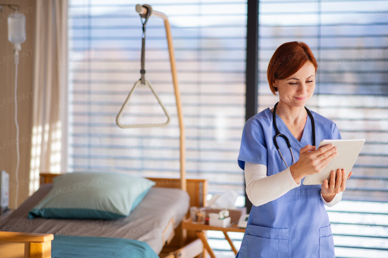 A portrait of female doctor or nurse standing in hospital room, using tablet.