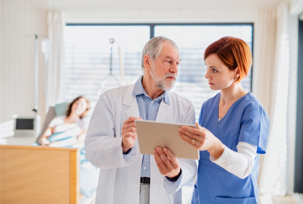 Front view of doctor and nurse with tablet discussing issues in hospital room.