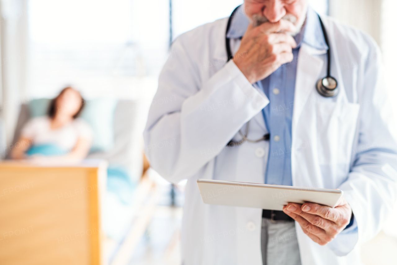 An unrecognizable senior male doctor standing in hospital room, using tablet.