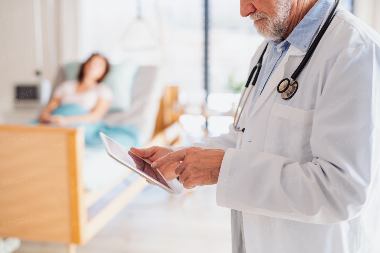 Unrecognizable senior doctor standing in hospital room, using tablet.