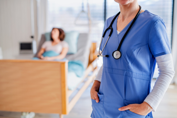 Midsection of unrecognizable doctor standing in hospital room, patient in the background.