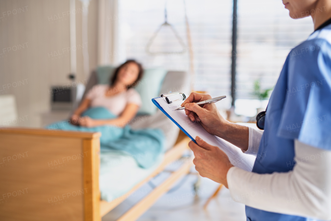 An unrecognizable doctor or nurse standing in hospital room, holding clipboard.