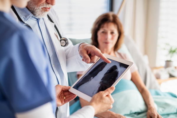 Senior male doctor with nurse examining a woman patient in hospital, checking X-ray.