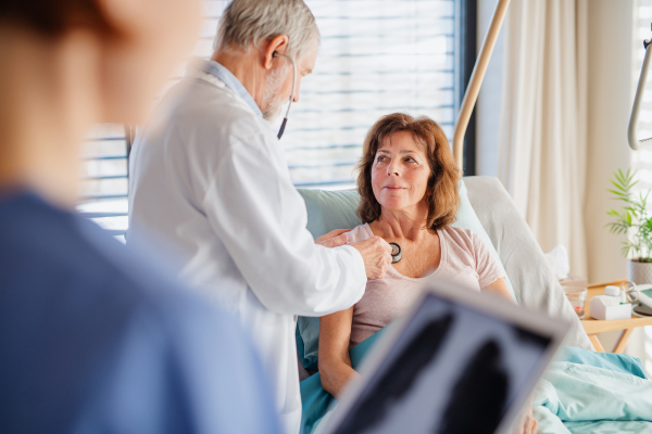 A senior doctor and nurse examining a woman patient in hospital.