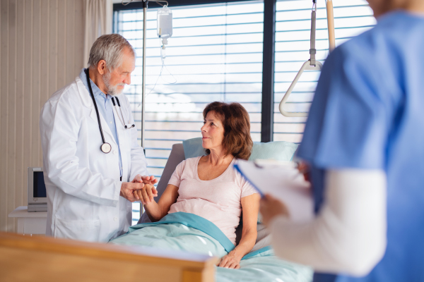 Man doctor and nurse examining senior patient in bed in hospital.