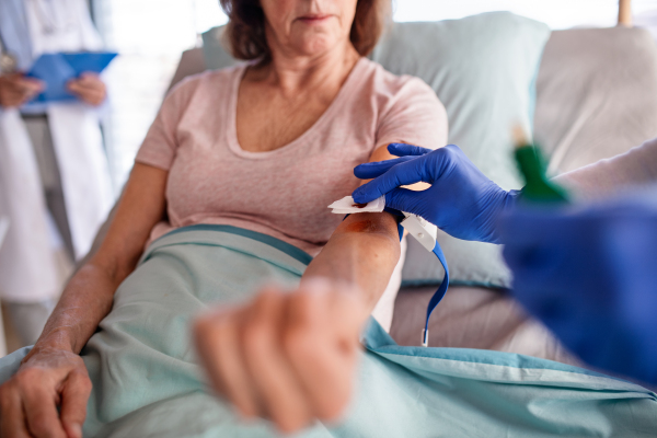 Midsection of unrecognizable nurse with patient in bed in hospital, blood taking