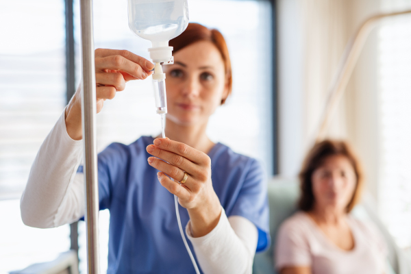 A front view of nurse with IV drip and patient in bed in hospital room.