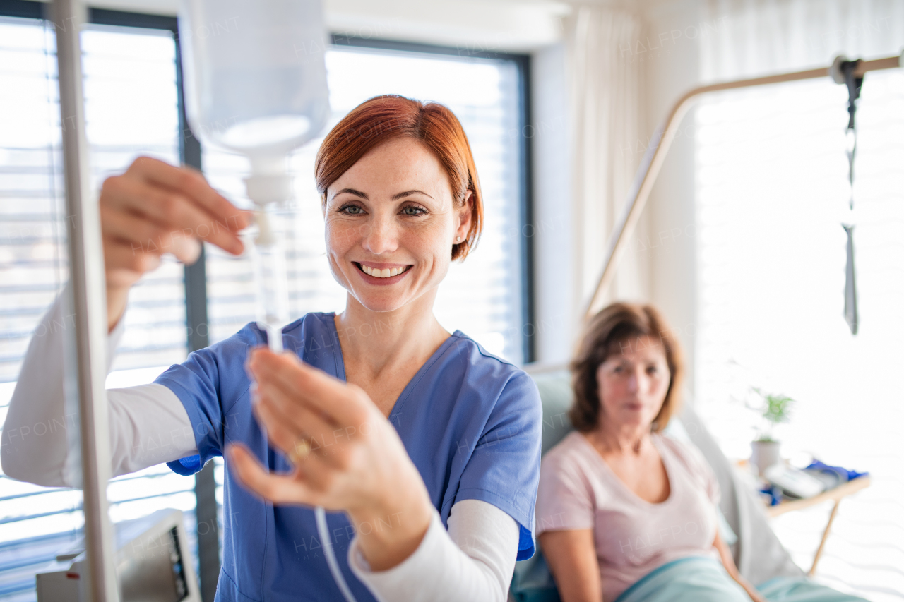 A front view of nurse with IV drip and patient in bed in hospital room.