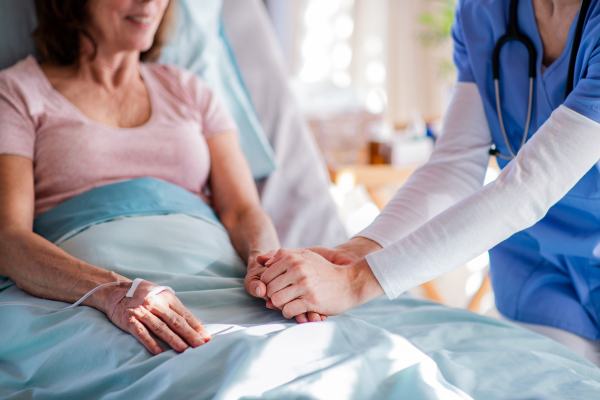 Unrecognizable doctor talking to senior patient in bed in hospital, midsection.