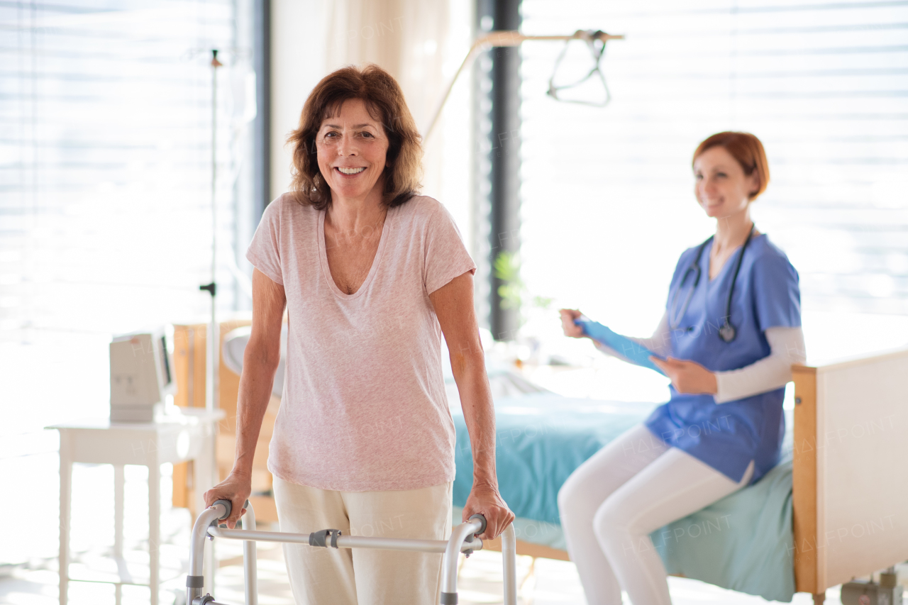 A senior woman patient with walking frame and nurse in hospital room.