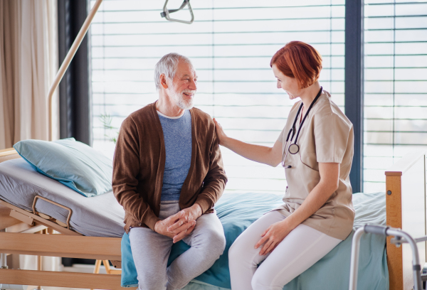 A friendly female doctor talking to senior patient in bed in hospital.