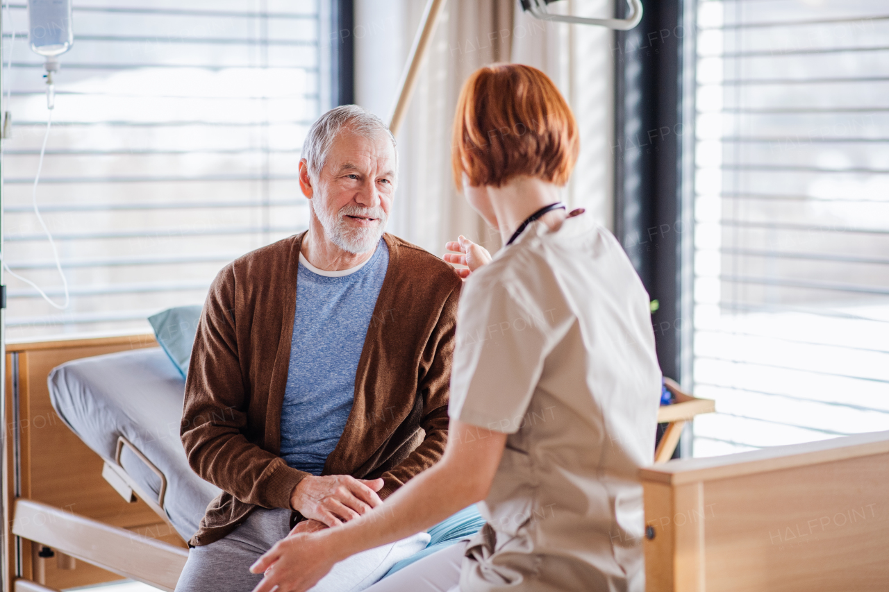 A friendly female doctor talking to senior patient in bed in hospital.