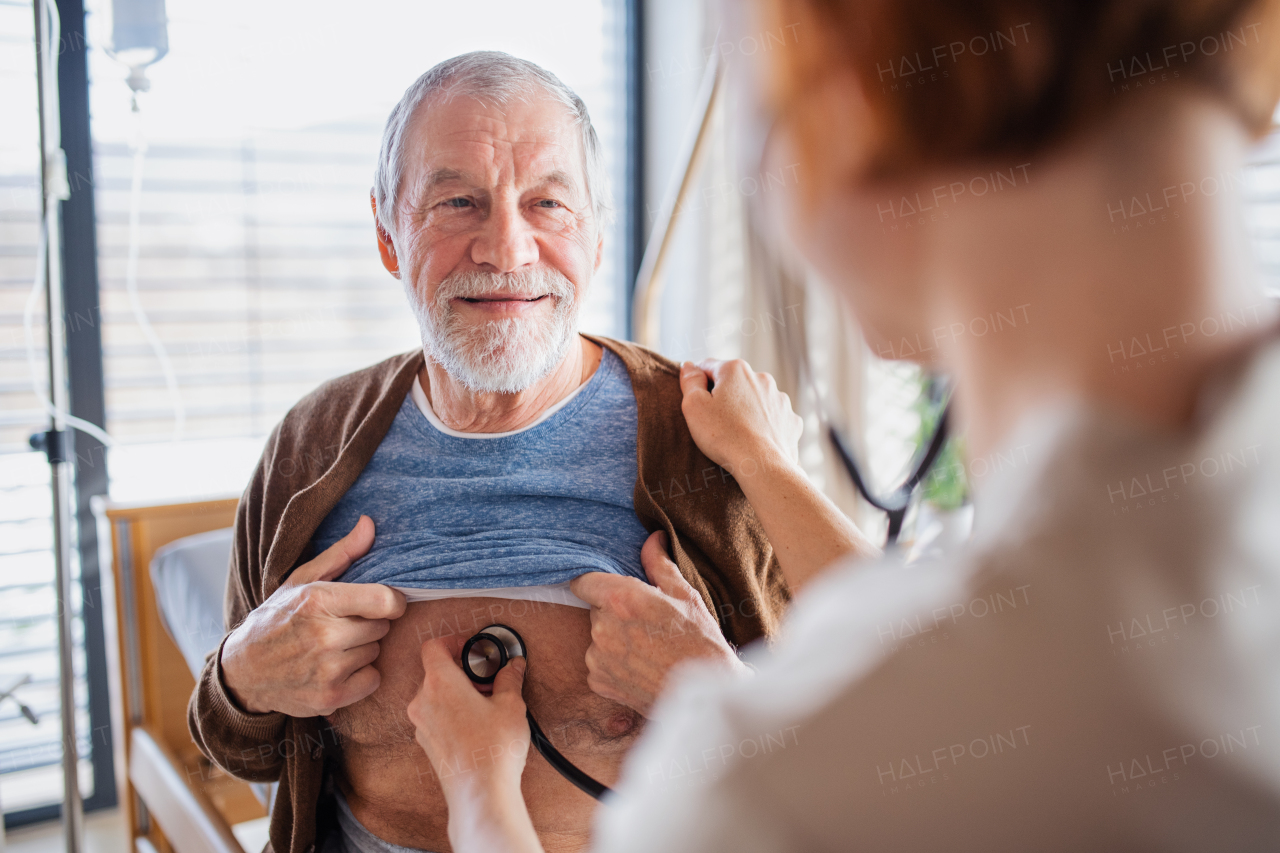 A friendly female doctor examinig a senior patient with stethoscope in bed in hospital.