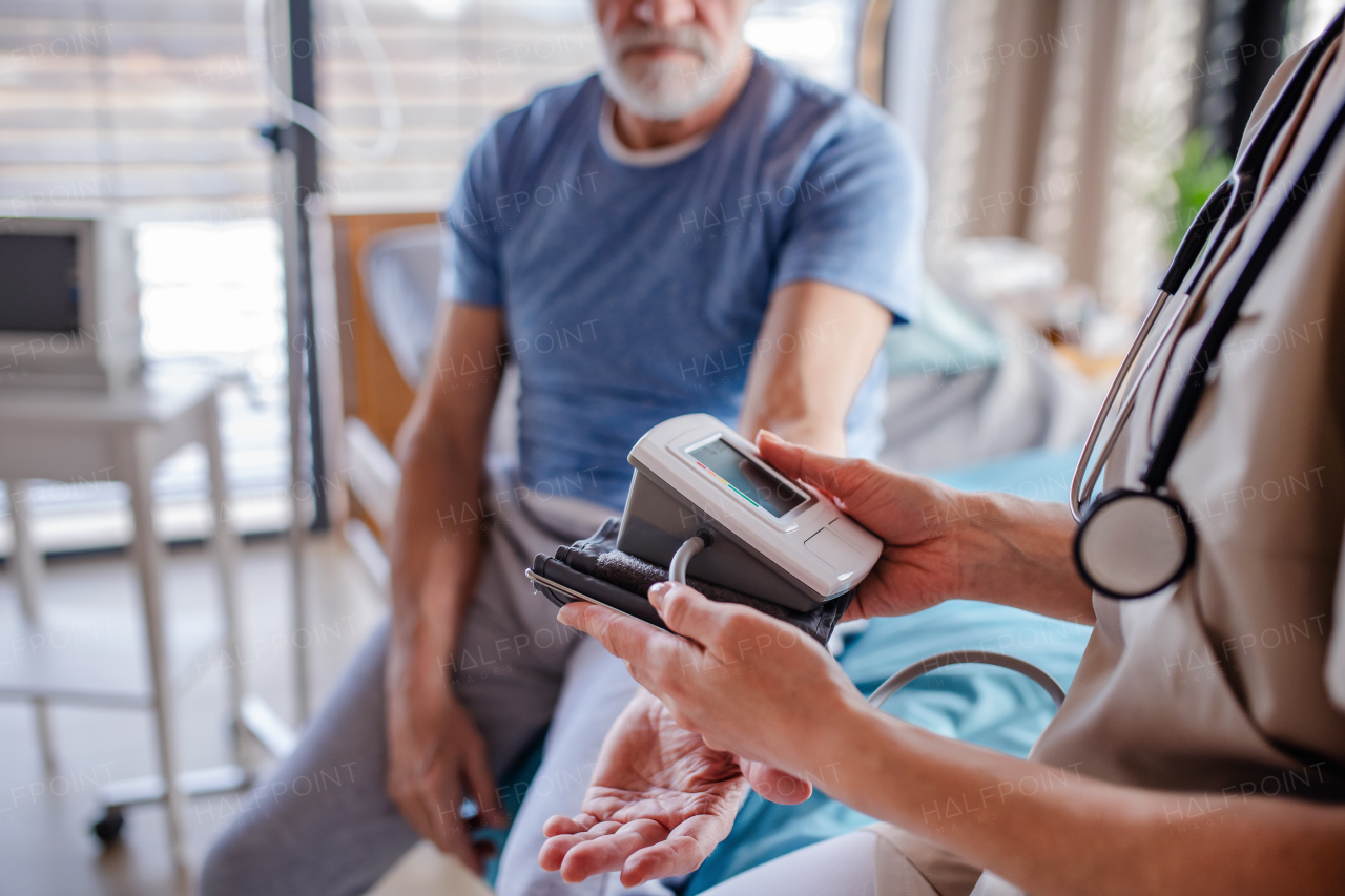 Unrecognizable female doctor examining senior patient in bed in hospital, midsection.