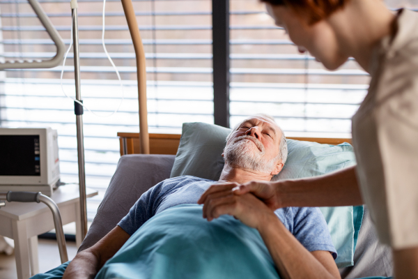 Unrecognizable female doctor examining senior patient in bed in hospital, midsection.