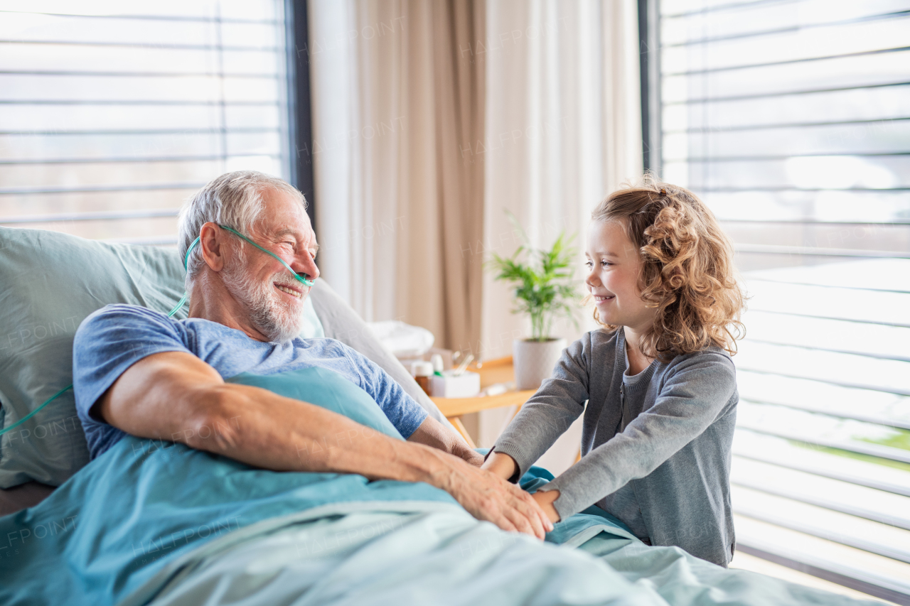 A cheerful small girl visiting ill grandfather in bed in hospital room.