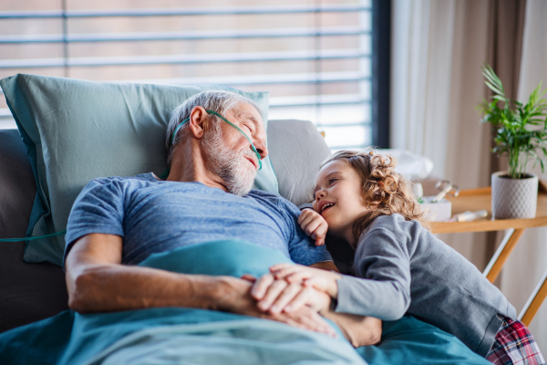 A cheerful small girl visiting ill grandfather in bed in hospital room.