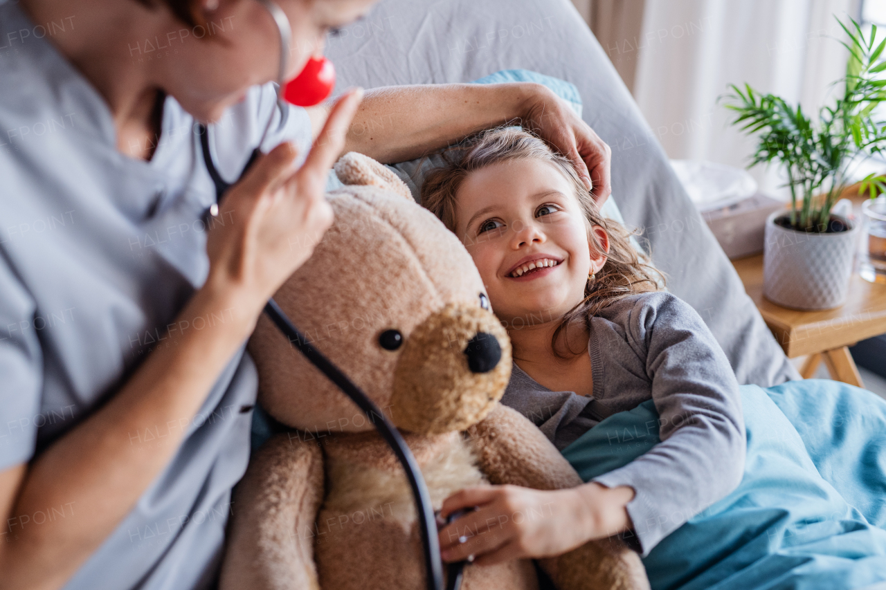 Friendly female doctor with stethoscope examining small girl in bed in hospital.