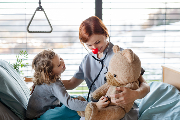 Friendly female doctor with stethoscope examining small girl in bed in hospital.