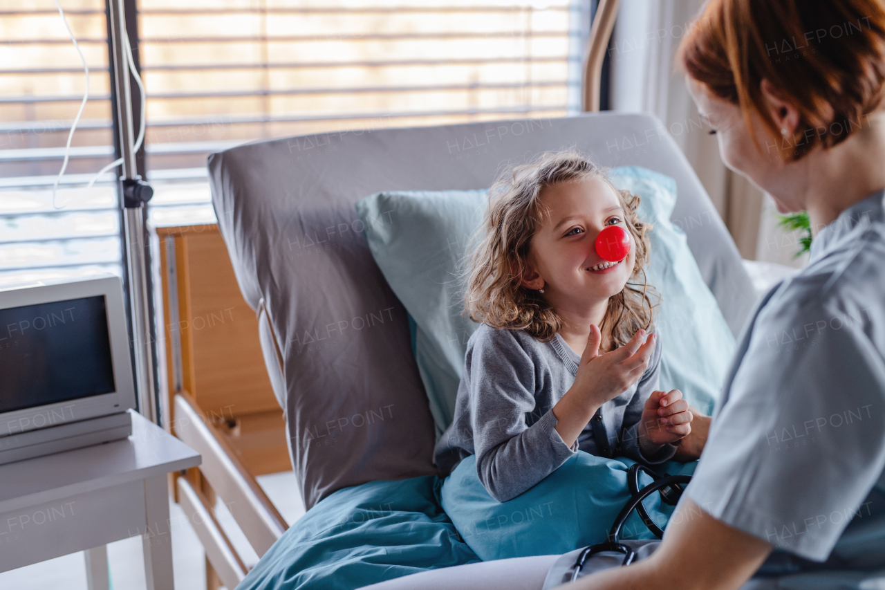 Friendly female doctor with stethoscope examining small girl in bed in hospital.