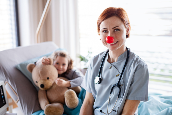 Friendly female doctor with stethoscope examining small girl in bed in hospital.