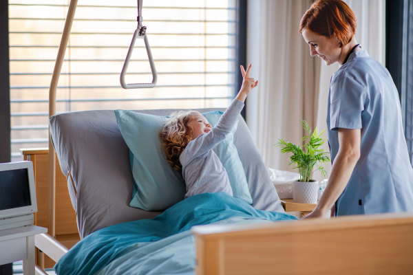 Friendly female woman doctor examining small girl in bed in hospital.