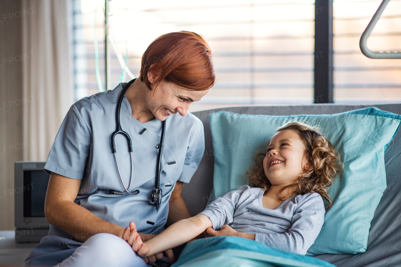 Friendly female doctor with stethoscope examining small girl in bed in hospital.