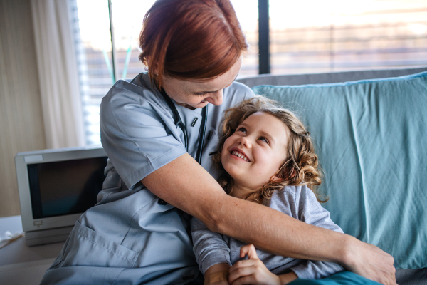 Friendly female doctor with stethoscope talking to small girl in bed in hospital.