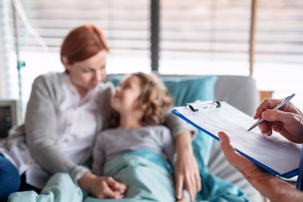 Unrecognizable doctor examining a small hospitalized girl with mother in hospital, writing.