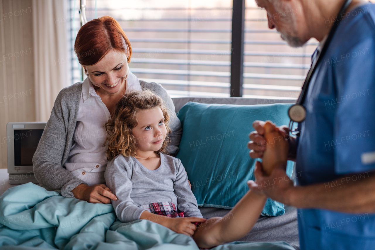 Senior doctor examining a small hospitalized girl with mother in hospital.