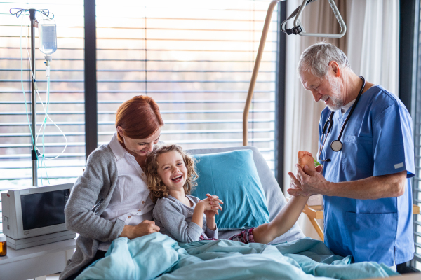 Senior doctor examining a small hospitalized girl with mother in hospital.