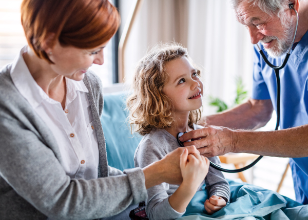 Senior doctor with stethoscope examining a small hospitalized girl with mother in hospital.