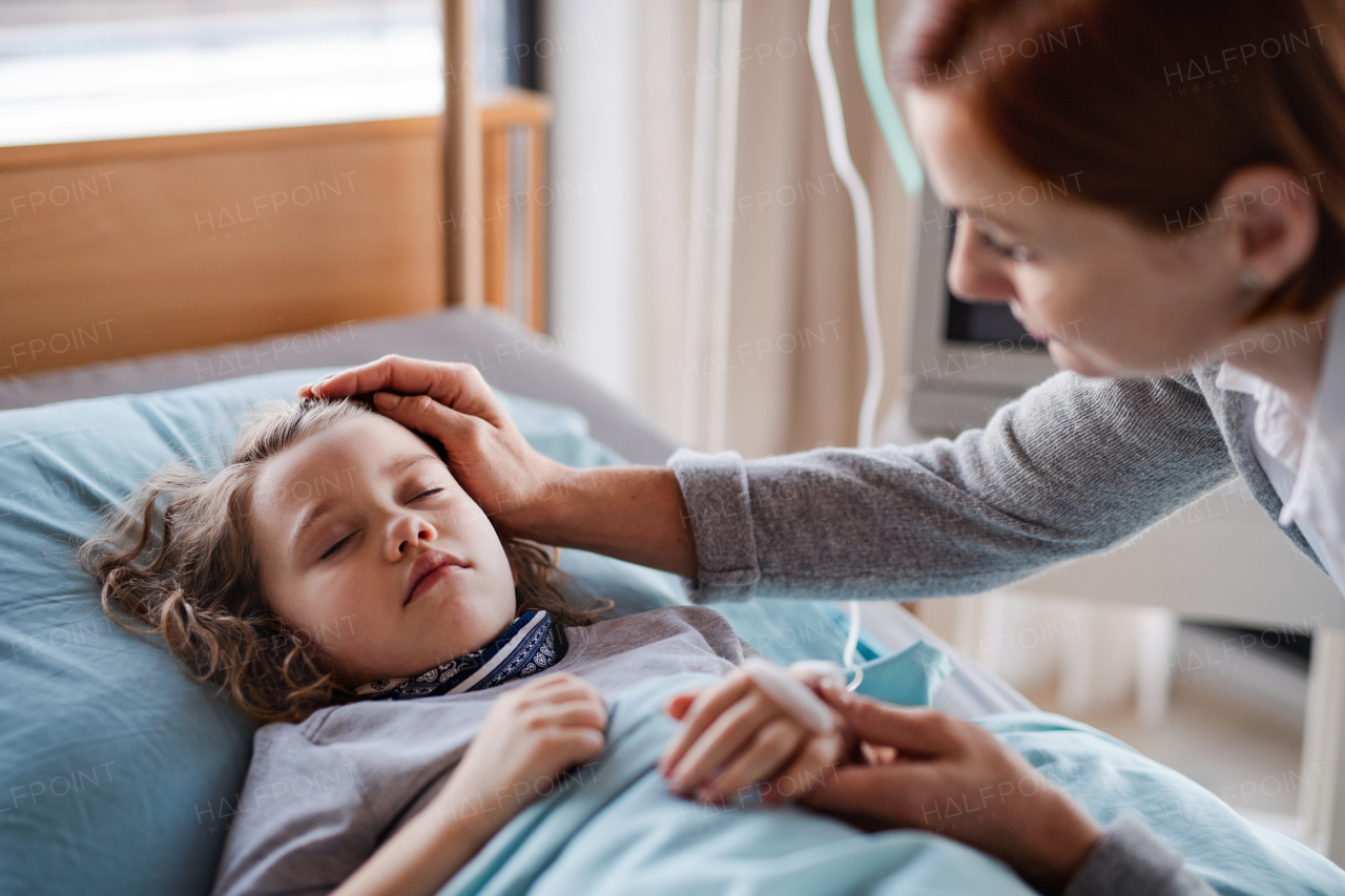 Caring mother visiting sleeping small girl daughter in bed in hospital.