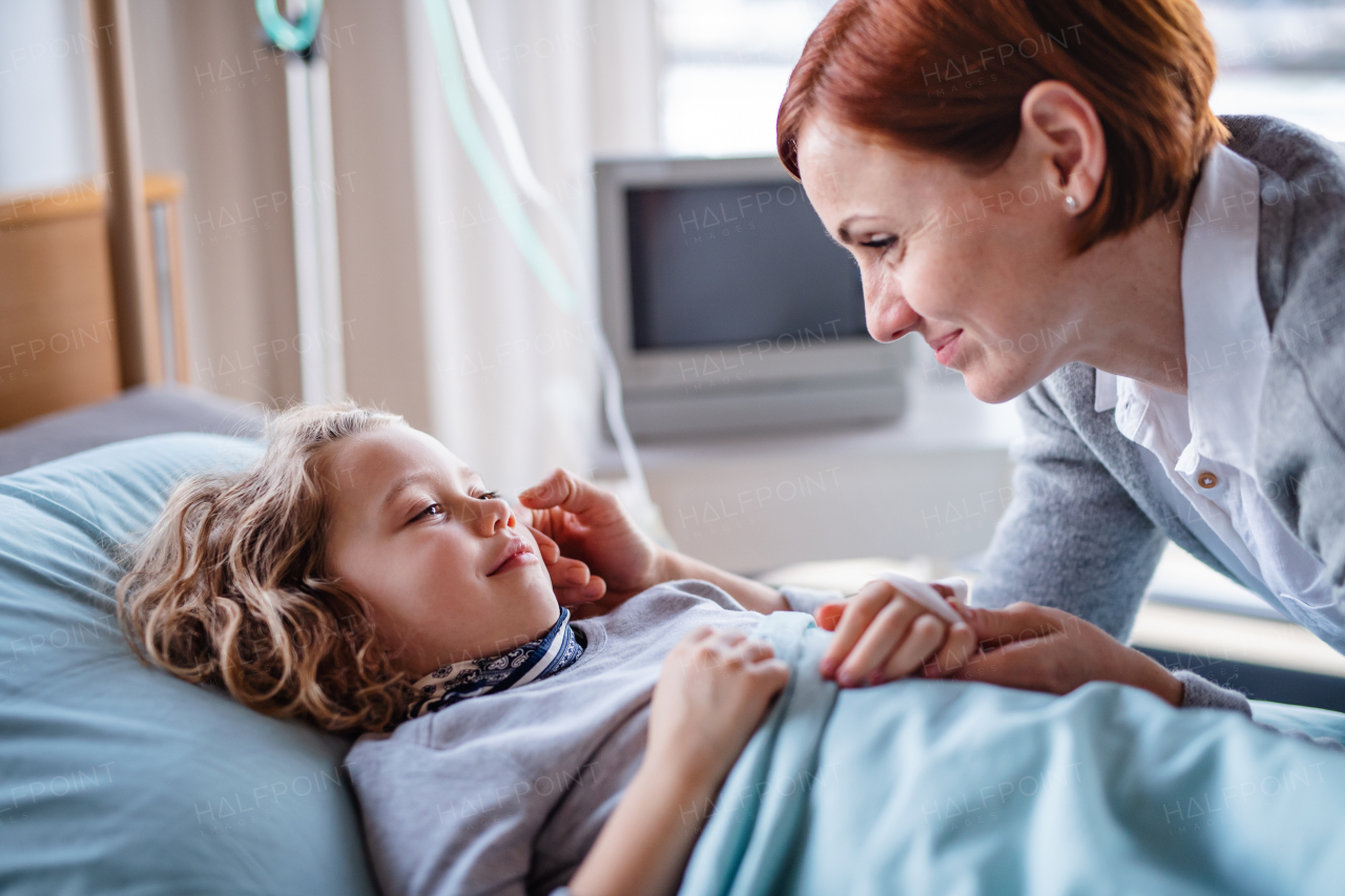 Caring mother visiting small girl daughter in bed in hospital, midsection.